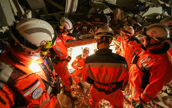 Sechs Mitglieder der Rettungskette stehen in den Trümmern eines Gebäudes und sprechen miteinander.