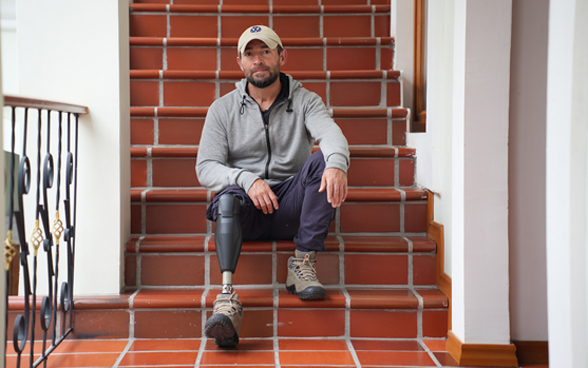 Andres Betancourt est assis sur un escalier. Il porte une prothèse de jambe.