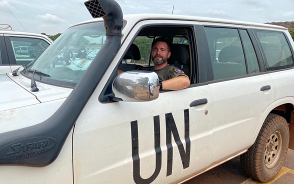  A male UN police officer at the wheel of a white car marked 'UN'.