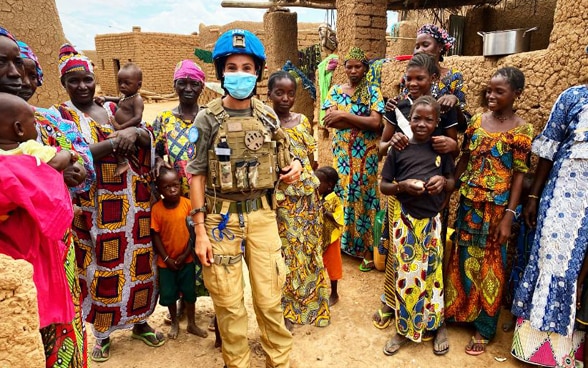  Photograph of a woman police officer wearing a face mask surrounded by Malian women and children  in a village in the Mopti region 