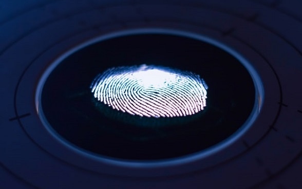 Un’impronta digitale illuminata dal basso su una lastra di vetro scura. 