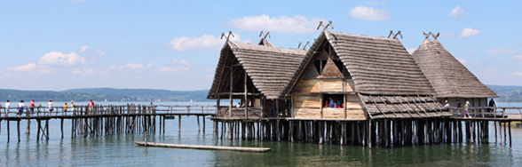 Photo of three pile dwellings in the water and footbridges with visitors.