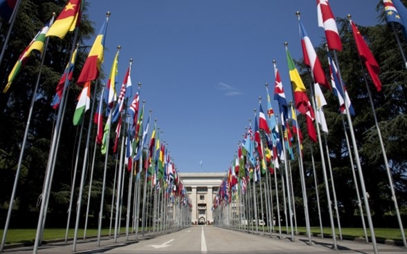 Blick auf das Gebäude der Vereinten Nationen in Genf mit Fahnen verschiedener Staaten.