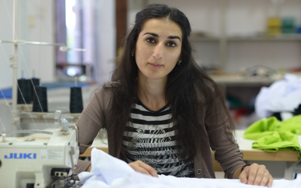 A young woman sitting at a sewing machine, holding material in her hand.