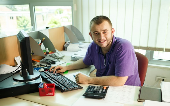 A young man sitting in an office in front of a computer.