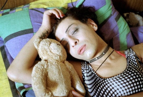 a transgender woman lying in bed with a teddy bear