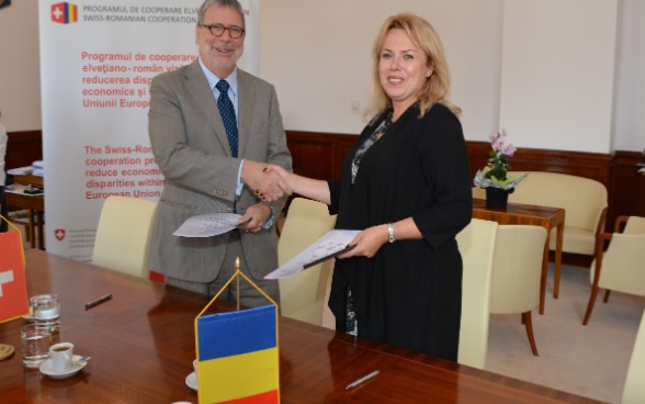 Ambassador Urs Herren and Minister Aura Dragu exchange the signed documents 