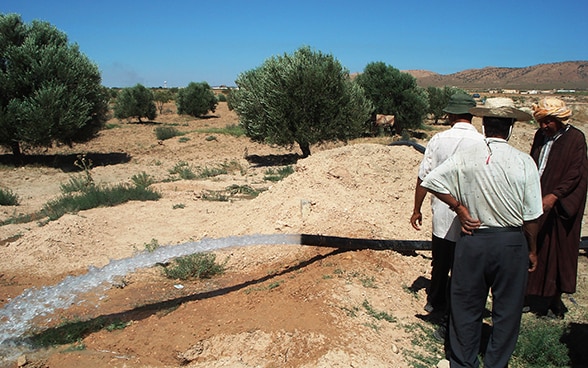 Trois hommes à côté d'une conduite d'eau. 