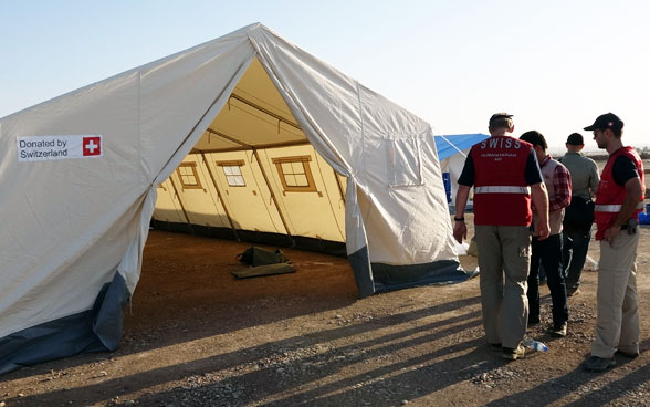 le personnel humanitaire devant une tente montée, avec l’inscription « Donated by Switzerland ». 