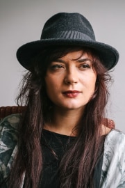 The Albanian musician Elina Duni sitting on a chair, wearing a hat. 