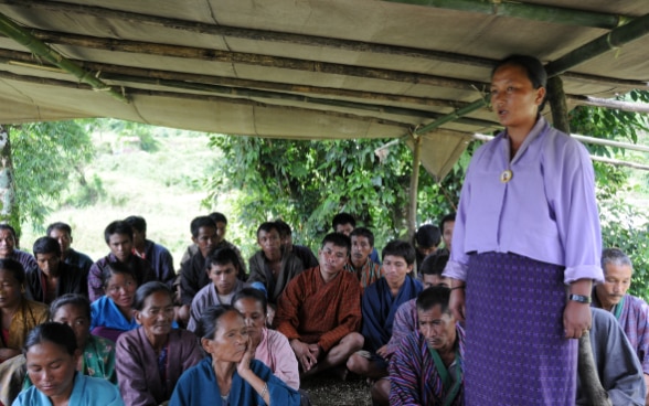 Eine Frau spricht an einer Dorfversammlung.