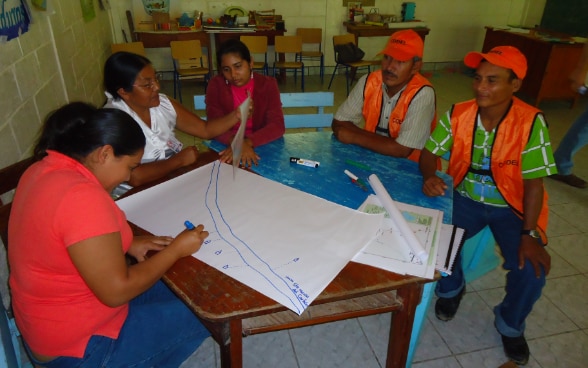Un groupe de Honduriens est assis autour d’une table de travail. Une femme dessine un croquis.