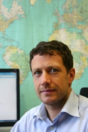 Markus Bürli sitzt in seinem Büro vor einer Weltkarte.