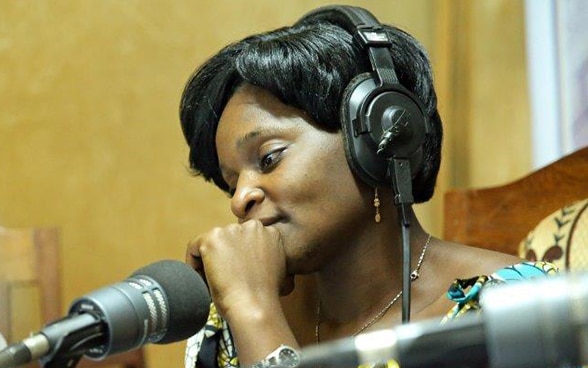 Une femme africaine s’exprime au micro d’un studio de radio.