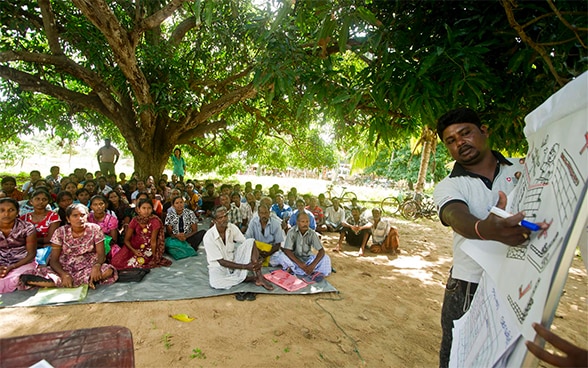 Anhand einer Schautafel berät sich ein Experte der DEZA in Sri Lanka mit etwa 50 Dorfbewohnern, um die notwendigen Wiederaufbaumassnahmen festzulegen.