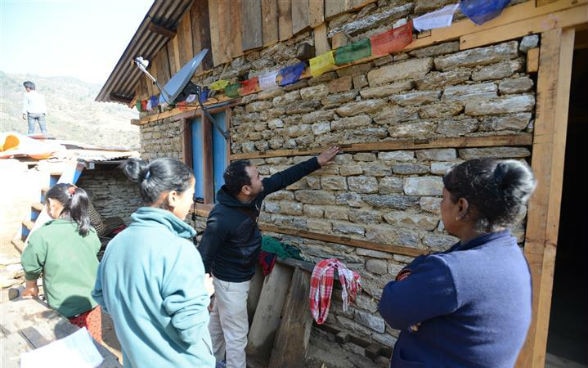 Un maçon parle à des villageoises devant leur maison