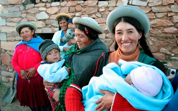 Vier Bolivianerinnen, drei mit einem Kind im Arm.