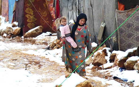 Una mujer en un campo de refugiados sirio llevando en brazos a un niño.