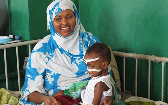 A woman sits on a hospital bed with her child on her lap. Both are suffering from severe malnutrition. They are being treated in a hospital in Mogadishu, Somalia.