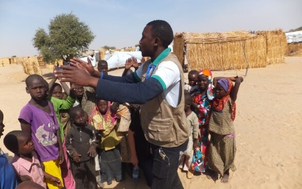 A staff member of COOPI speaking to a group of children in a camp.