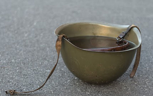 Ein Militärhelm liegt mit der Innenseite gegen den Himmel gerichtet draussen auf dem Asphalt. 