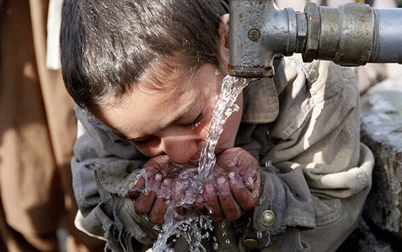 A young boy in Afghanistan drinking water from a fountain.