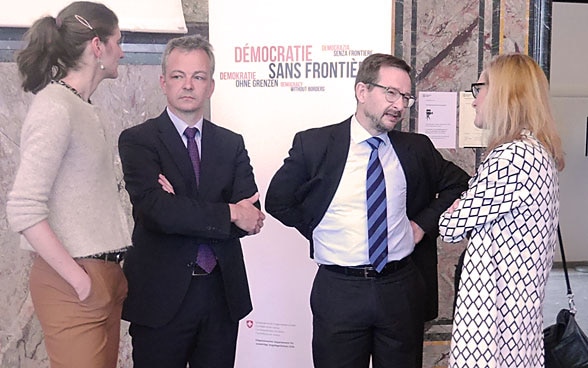 Prof. Daniel Kübler und Botschafter Thomas Greminger stehen mit zwei Podiumsteilnehmerinnen in der Aula und unterhalten sich. 