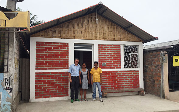 Hausbesitzer vor ihrem neuen Haus in Begleitung eines Mitarbeiters der Humanitären Hilfe der DEZA.