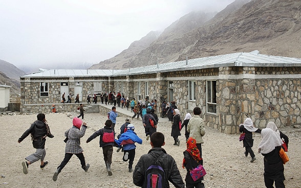 Eine Gruppe von Kindern läuft auf ein Schulgebäude in einer Gebirgsregion zu.