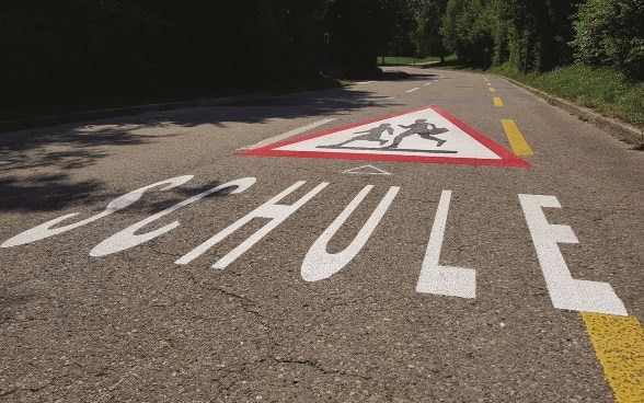 Road marking with the word school and the school children symbol.