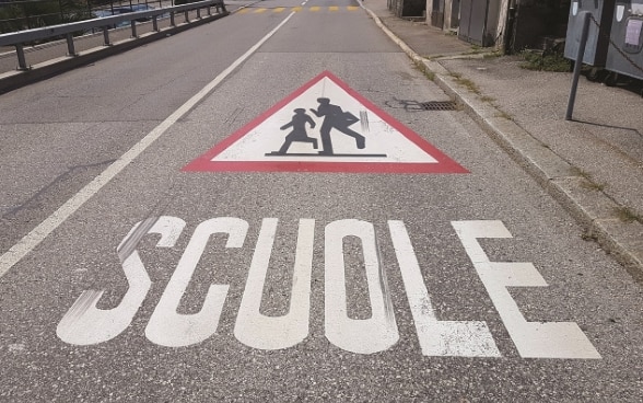Segnaletica orizzontale che raffigura la scritta «scuole» e il relativo cartello su una strada.