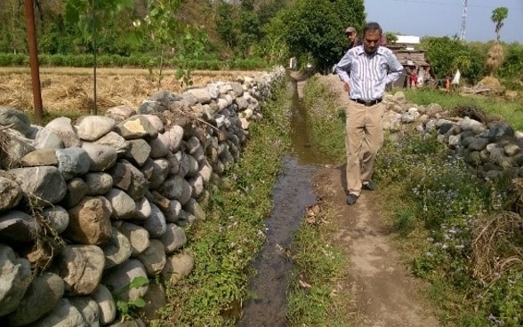 Deux hommes examinent l’état d’un canal d’irrigation qui longe un mur de pierres.