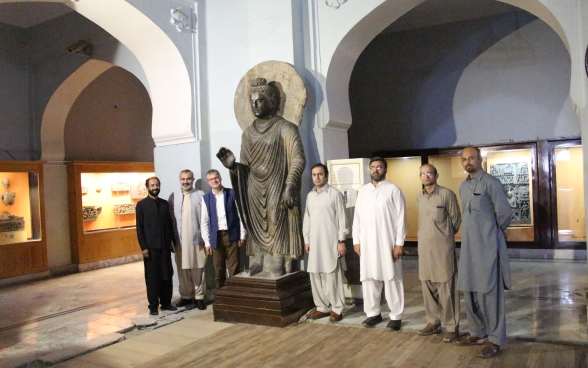 Einige Männer stehen links und rechts von der Buddha-Skulptur in einem Saal des Museums von Peshawar versammelt.