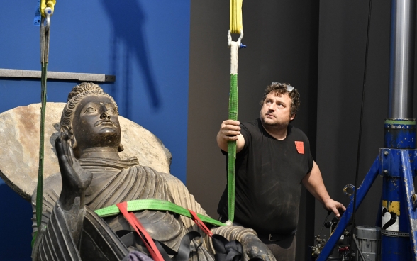 Ein Mitarbeiter des Museums Rietberg überwacht das Aufrichten der an zwei Gurten hängenden Buddha-Skulptur.