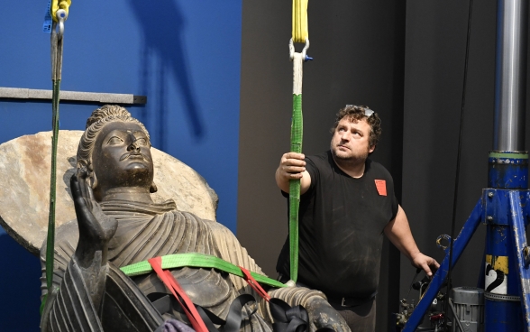 Un collaboratore del Museo Rietberg monitora il processo con il quale la statua, fissata con due cinghie, viene eretta in posizione verticale.