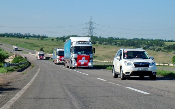 Lastwagen mit Schweizer Flaggen auf der Motorhaube brausen durch die ukrainische Steppe. 