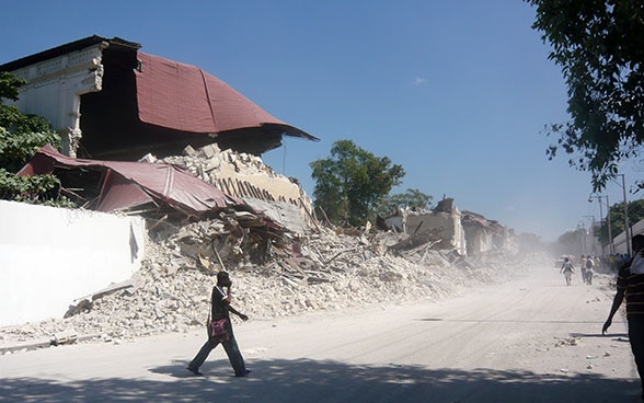A man walking past a group of houses reduced to rubble. 