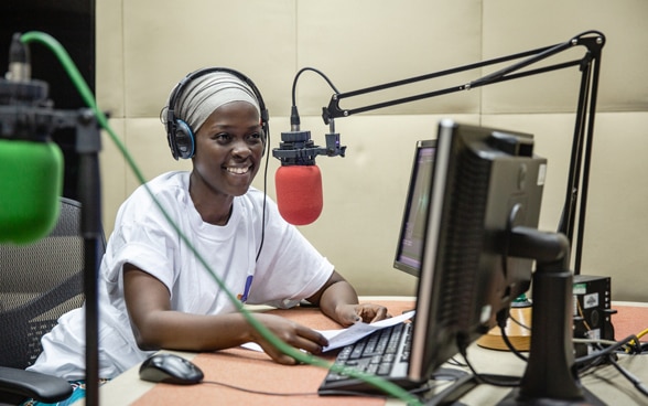 Eine afrikanische Radiomoderatorin macht eine unterhaltsame Radiosendung. Dazu benutzt sie ein rotes Mikrofon und einen Computer.