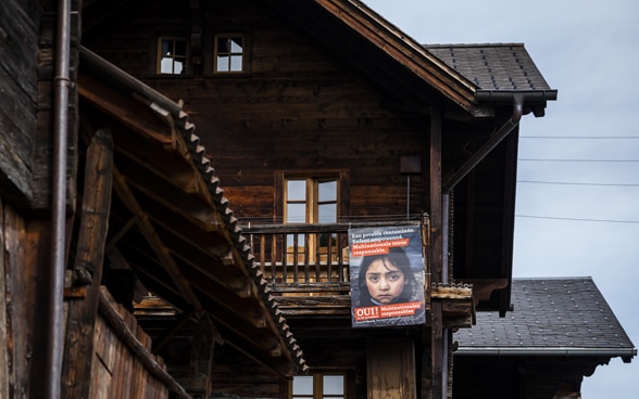 An orange referendum poster for the 'Responsible Business Initiative' on an old mountain barn made of dark wood.