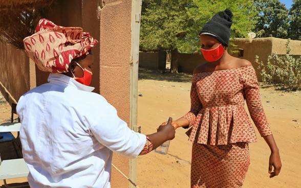 Zwei afrikanische Frauen tragen im aufgrund von Covid-19 Masken und desinfizieren sich die Hände.