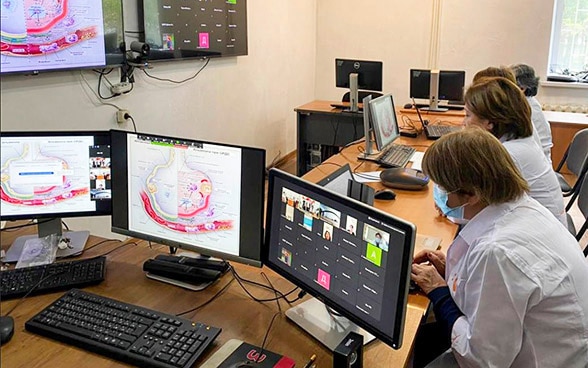 In a room with many screens, medical staff work on computers.