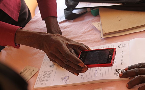 A woman uses her mobile phone to scan a QR code printed on a sheet of paper.