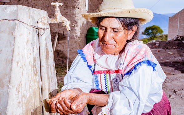 A Bolivian woman washes her hands at a tap.