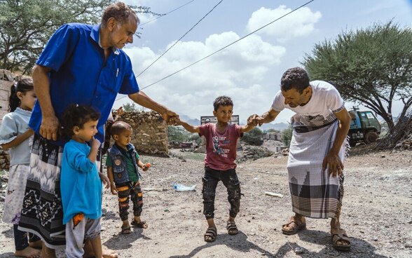 Due uomini tengono per mano un bambino che non è in grado di camminare da solo.