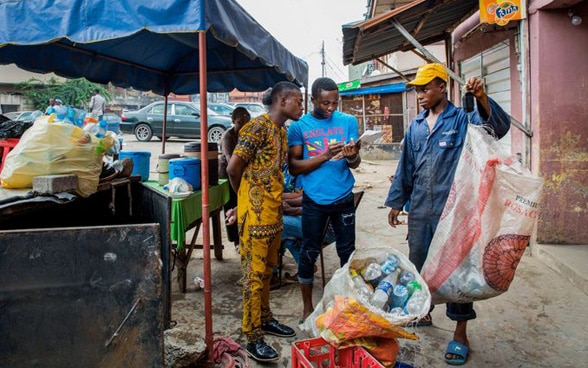 In der nigerianischen Metropole Lagos wiegen Männer ihre gesammelten Plastikflaschen und tragen das Gewicht an der Recycling-Sammelstelle ein.