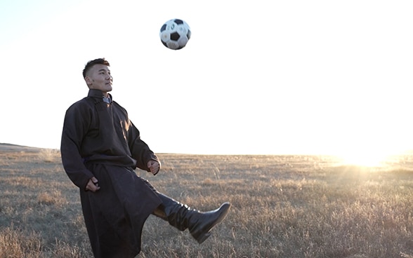 A man kicking a football on the Mongolian steppe.