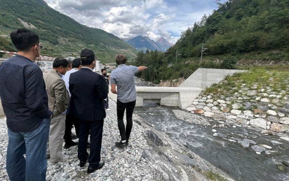 Par des gestes, un intervenant donne des explications aux délégations asiatiques, à proximité d’un barrage.