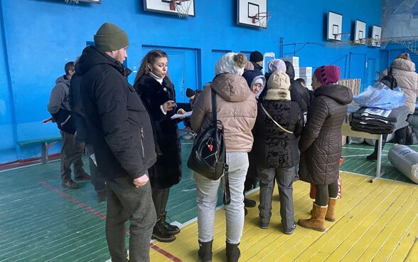 A woman talks to people arriving in a gymnasium that has been converted into an emergency shelter. 