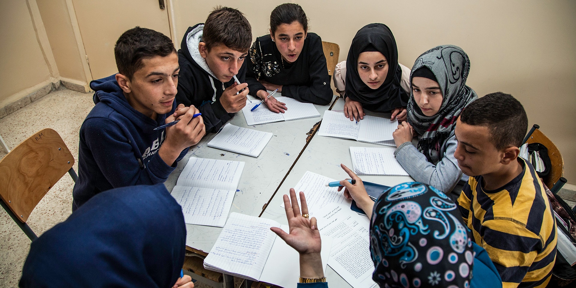 A group of young people are sitting around a table. Together they are doing schoolwork.