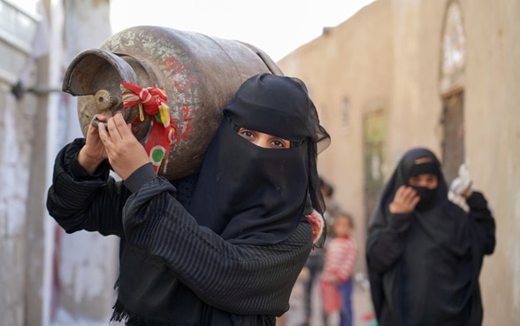 Two women carrie a gas cylinder on her shoulder and go to search for gas on the black market.